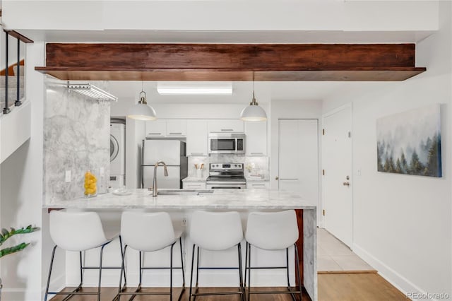 kitchen featuring stainless steel appliances, a peninsula, white cabinetry, a kitchen breakfast bar, and stacked washing maching and dryer