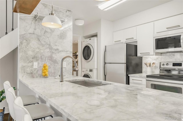 kitchen featuring stacked washer and clothes dryer, white microwave, freestanding refrigerator, a sink, and stainless steel range with electric stovetop