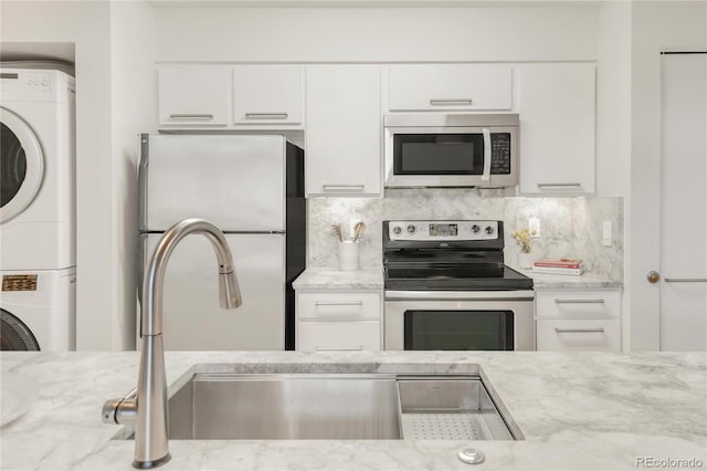 kitchen with light stone counters, stacked washer and dryer, white cabinets, appliances with stainless steel finishes, and decorative backsplash