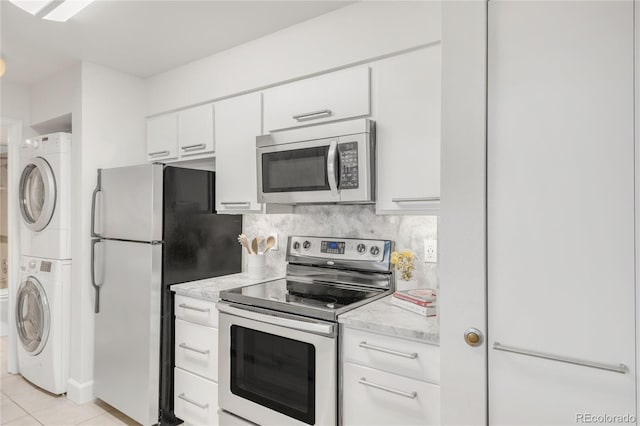 kitchen featuring light tile patterned floors, white cabinetry, appliances with stainless steel finishes, tasteful backsplash, and stacked washer and clothes dryer