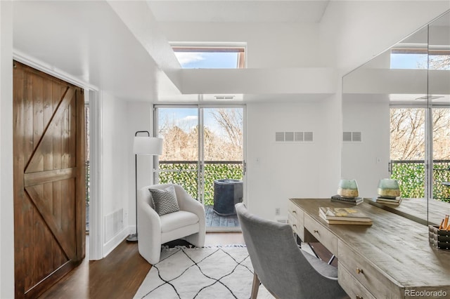 office with a wealth of natural light, a barn door, visible vents, and wood finished floors