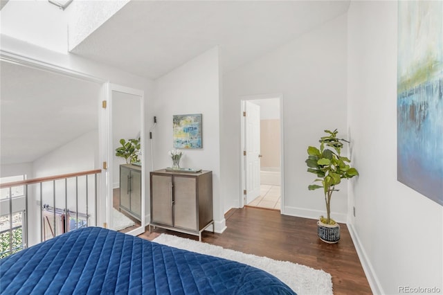 bedroom with baseboards, vaulted ceiling, wood finished floors, and ensuite bathroom