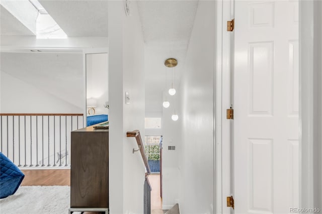 hallway with a textured ceiling, wood finished floors, and an upstairs landing