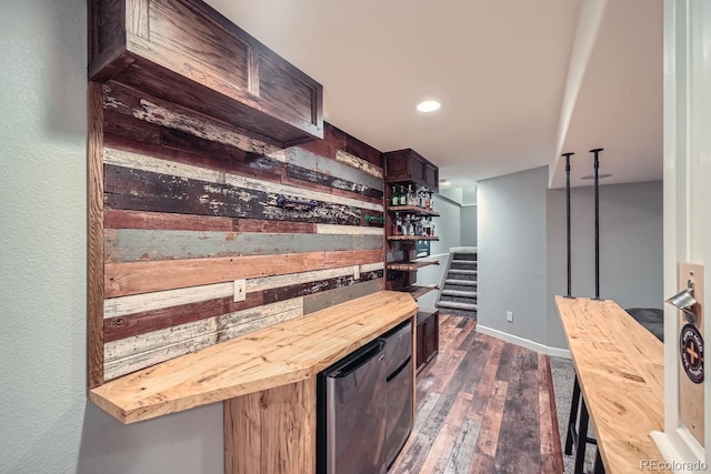 bar featuring dark wood-type flooring, wooden counters, wooden walls, and dark brown cabinets