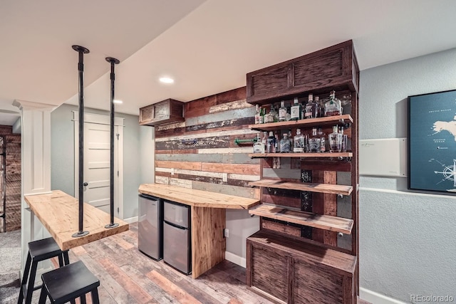 bar featuring dark brown cabinets, light hardwood / wood-style floors, wooden counters, and refrigerator