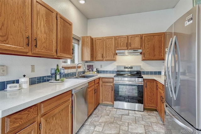 kitchen with a sink, appliances with stainless steel finishes, stone finish floor, under cabinet range hood, and brown cabinets