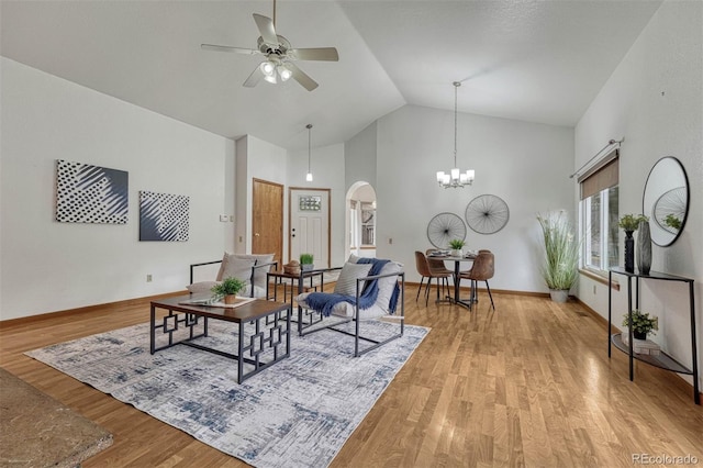 living area with high vaulted ceiling, arched walkways, ceiling fan with notable chandelier, and wood finished floors