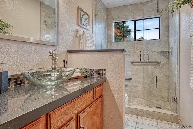 bathroom with toilet, a textured wall, vanity, tile patterned floors, and a stall shower