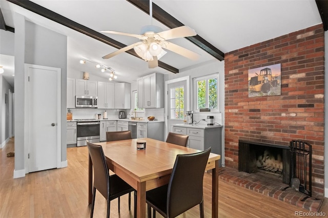 dining space with ceiling fan, lofted ceiling with beams, light wood-type flooring, and a fireplace