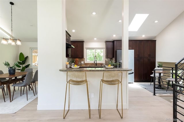 7453 E Jefferson Dr, Denver, CO 80237 - kitchen featuring freestanding refrigerator, dark brown cabinets, backsplash, a peninsula, and a skylight