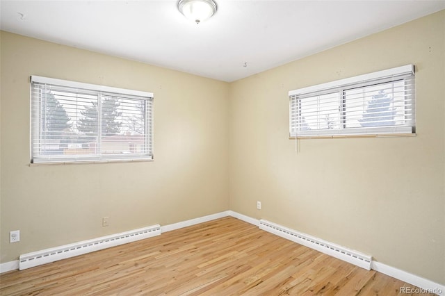 spare room featuring baseboard heating, a wealth of natural light, and light hardwood / wood-style flooring