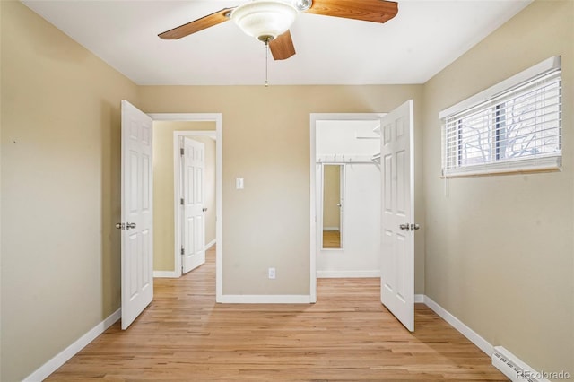 unfurnished bedroom with a walk in closet, ceiling fan, light hardwood / wood-style flooring, and a baseboard radiator