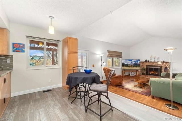 dining space with visible vents, baseboards, vaulted ceiling, a brick fireplace, and light wood finished floors