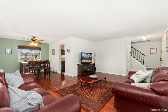 living area with a ceiling fan, stairway, baseboards, and wood finished floors