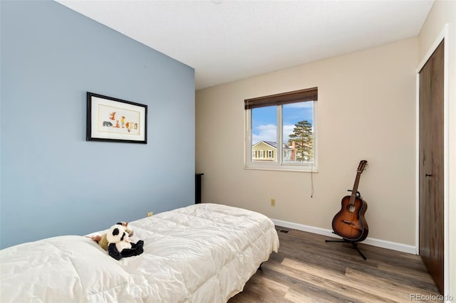 bedroom featuring a closet, wood finished floors, visible vents, and baseboards