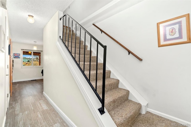 staircase with a textured ceiling, baseboards, and wood finished floors