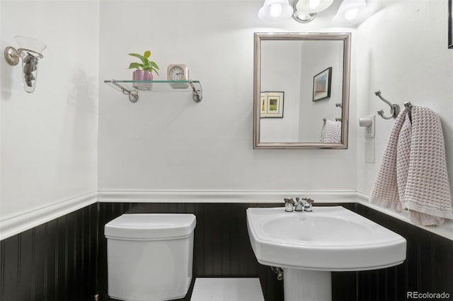 half bathroom featuring toilet, a wainscoted wall, and a sink