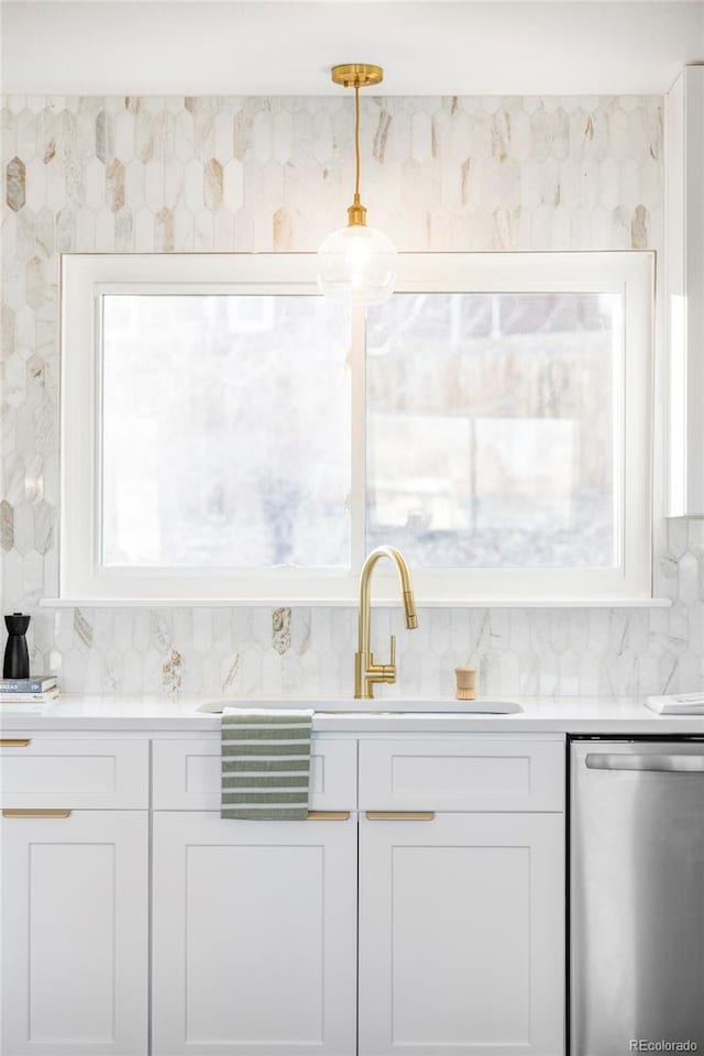 kitchen featuring tasteful backsplash, stainless steel dishwasher, sink, decorative light fixtures, and white cabinetry