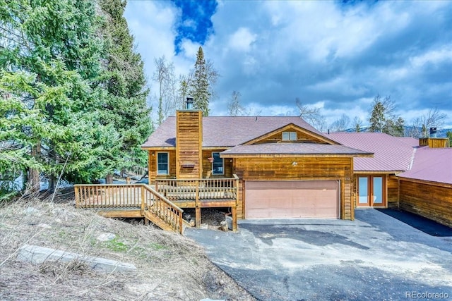 cabin featuring a garage, aphalt driveway, a wooden deck, and a chimney