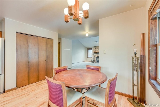 dining room featuring a fireplace, vaulted ceiling, baseboards, light wood finished floors, and a chandelier