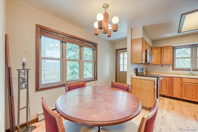 dining room featuring a healthy amount of sunlight, a baseboard heating unit, light wood-type flooring, and a chandelier