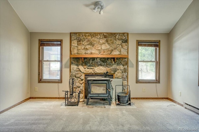 unfurnished living room with baseboards, a wood stove, carpet, and a baseboard radiator