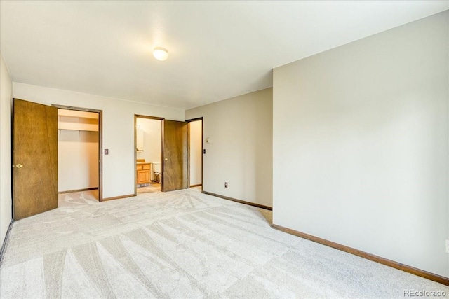 unfurnished bedroom featuring baseboards, a closet, a spacious closet, ensuite bathroom, and light carpet