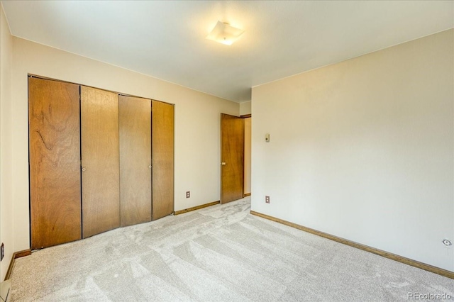 unfurnished bedroom with a closet, baseboards, and light carpet