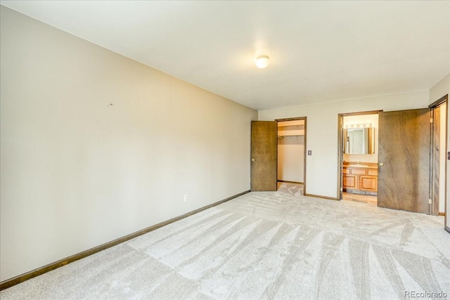 unfurnished bedroom with baseboards, a closet, a spacious closet, ensuite bathroom, and light carpet