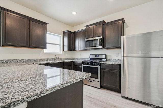 kitchen with light stone counters, sink, dark brown cabinetry, and appliances with stainless steel finishes