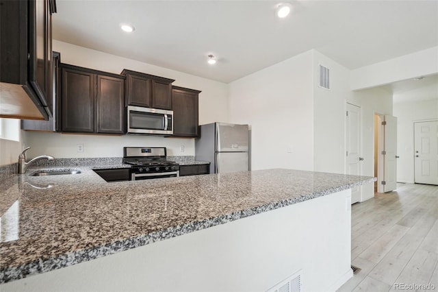 kitchen featuring sink, stone countertops, appliances with stainless steel finishes, kitchen peninsula, and light hardwood / wood-style floors