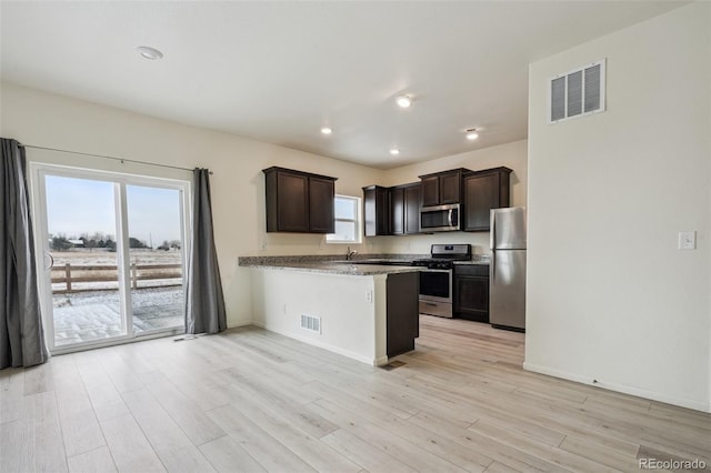 kitchen featuring dark brown cabinetry, light wood-type flooring, kitchen peninsula, stainless steel appliances, and light stone countertops