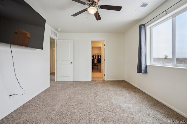 unfurnished bedroom with a spacious closet, light colored carpet, ceiling fan, and a closet