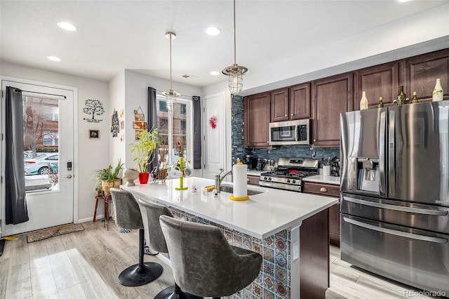 kitchen featuring pendant lighting, appliances with stainless steel finishes, an island with sink, decorative backsplash, and sink