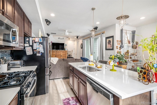 kitchen featuring appliances with stainless steel finishes, light hardwood / wood-style flooring, sink, ceiling fan, and a center island with sink