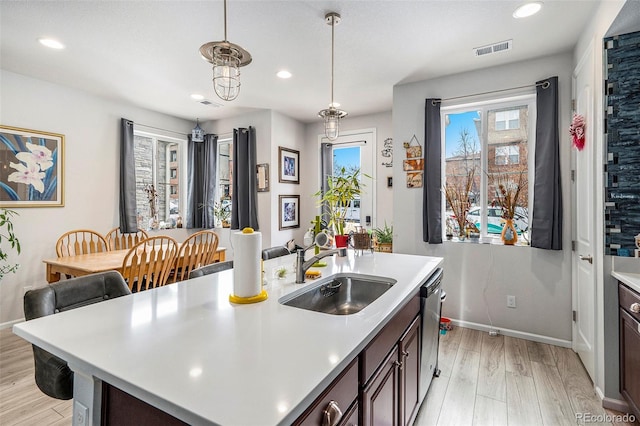 kitchen with a kitchen island with sink, dishwasher, hanging light fixtures, dark brown cabinetry, and sink