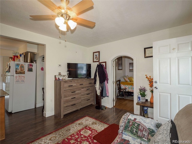 bedroom with arched walkways, dark wood-style floors, freestanding refrigerator, and a ceiling fan