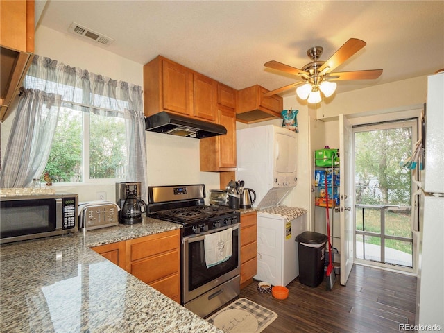 kitchen featuring visible vents, brown cabinetry, stacked washing maching and dryer, stainless steel appliances, and under cabinet range hood