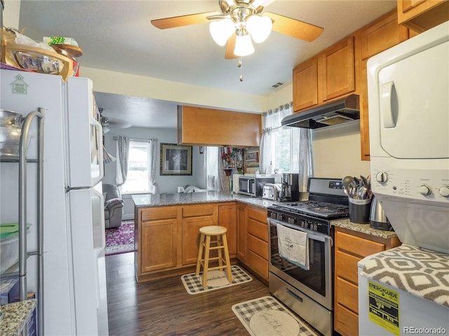 kitchen featuring under cabinet range hood, a peninsula, dark wood-type flooring, appliances with stainless steel finishes, and stacked washer and clothes dryer