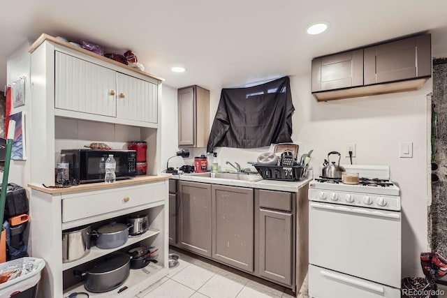 kitchen featuring black microwave, light tile patterned flooring, a sink, white gas range oven, and gray cabinets