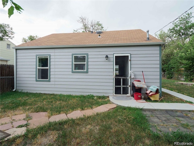 back of house with a yard, roof with shingles, and fence