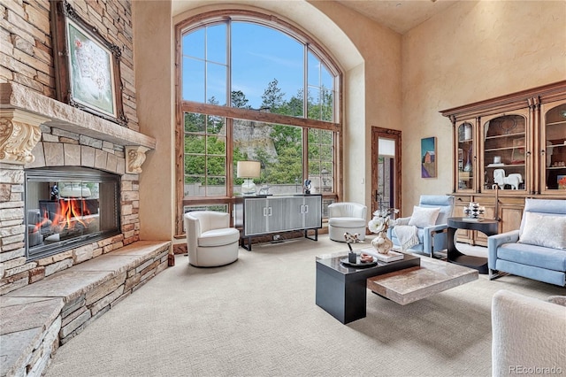 living room with a stone fireplace, a towering ceiling, and carpet floors