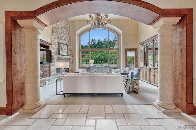 living room with a stone fireplace, a healthy amount of sunlight, a chandelier, and a high ceiling