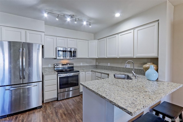 kitchen with a breakfast bar, appliances with stainless steel finishes, white cabinetry, light stone countertops, and kitchen peninsula