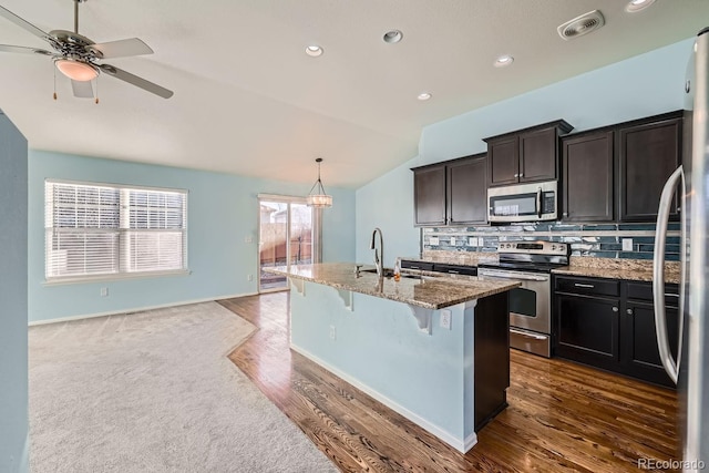 kitchen with pendant lighting, lofted ceiling, a kitchen island with sink, sink, and appliances with stainless steel finishes