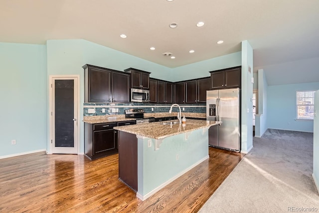 kitchen with a center island with sink, sink, light stone countertops, appliances with stainless steel finishes, and dark hardwood / wood-style flooring