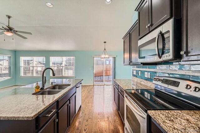 kitchen with tasteful backsplash, stainless steel appliances, sink, decorative light fixtures, and light hardwood / wood-style floors