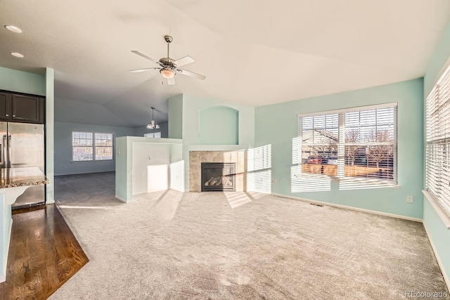 unfurnished living room featuring dark colored carpet, ceiling fan, a tiled fireplace, and vaulted ceiling