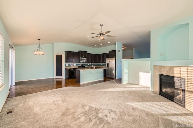 unfurnished living room with a tile fireplace, ceiling fan, dark carpet, and lofted ceiling