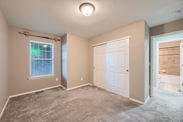 unfurnished bedroom with ensuite bathroom, carpet floors, a textured ceiling, and a closet